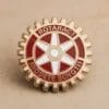 Un'elegante spilla Rotaract in rosso e oro, con la parola "rotatrici" in evidenza per il riconoscimento e l'orgoglio.