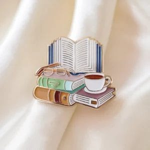 دبوس ساحر مصنوع من المينا يصور كتاباً ونظارة وكوب قهوة، مثالي لمحبي الكتب والأجواء المريحة للقراءة.