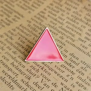 Spilla smaltata a forma di triangolo rosa con la scritta "Triangle Rouge" appoggiata sulla pagina di un libro aperto.
