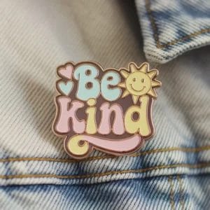 Una spilla con la scritta "Be Kind" in un carattere semplice e in grassetto, che promuove la gentilezza e la positività.