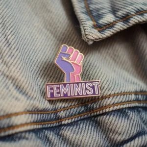 Spilla smaltata con la parola "Feminist" a caratteri cubitali, simbolo del sostegno ai diritti delle donne e all'uguaglianza di genere.