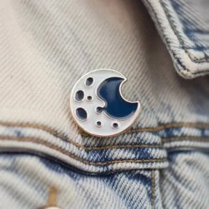 Una spilla a forma di luna blu, esposta su una giacca di jeans, mette in evidenza un accessorio di stile ispirato ai temi celesti.