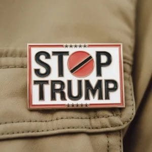 Spilla smaltata con la frase "Stop Trump" a caratteri cubitali, che promuove un messaggio politico contro Donald Trump.