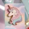 Spilla a forma di unicorno su un cartoncino con un vivace sfondo arcobaleno, che presenta un design stravagante e colorato.