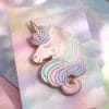 Spilla unicorno visualizzata su un cartoncino con un vivace sfondo arcobaleno.